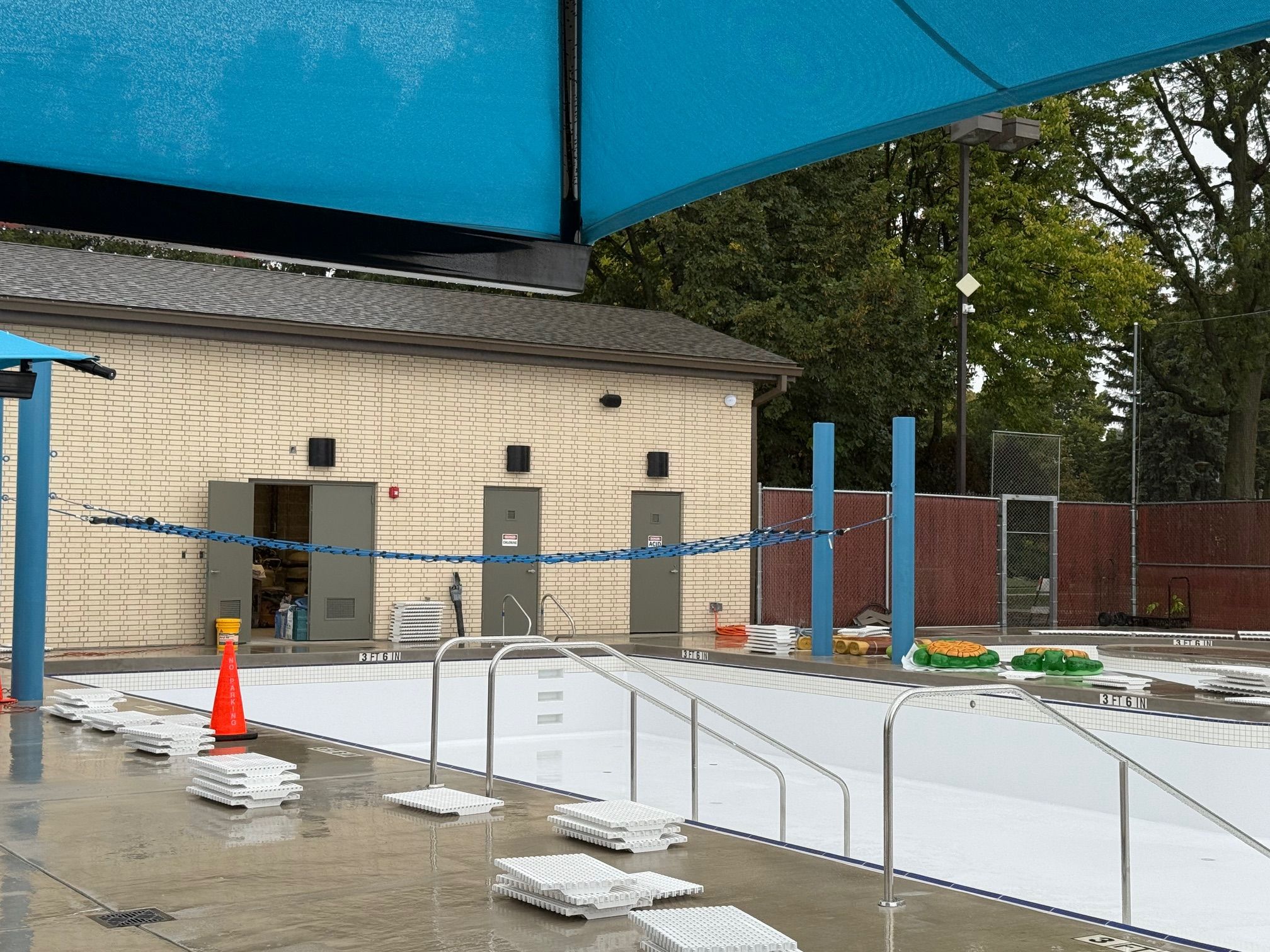Rehm Park & Pool under construction, featuring an empty pool basin with safety equipment and building in the background.