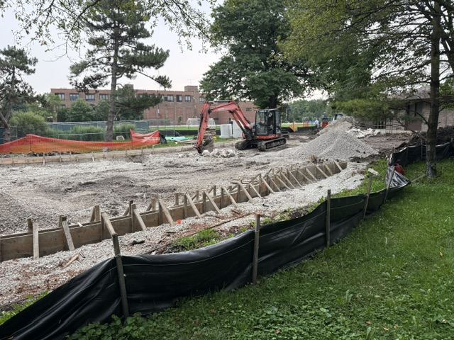 a large construction excavator works in a gravel area where field playground used to stand