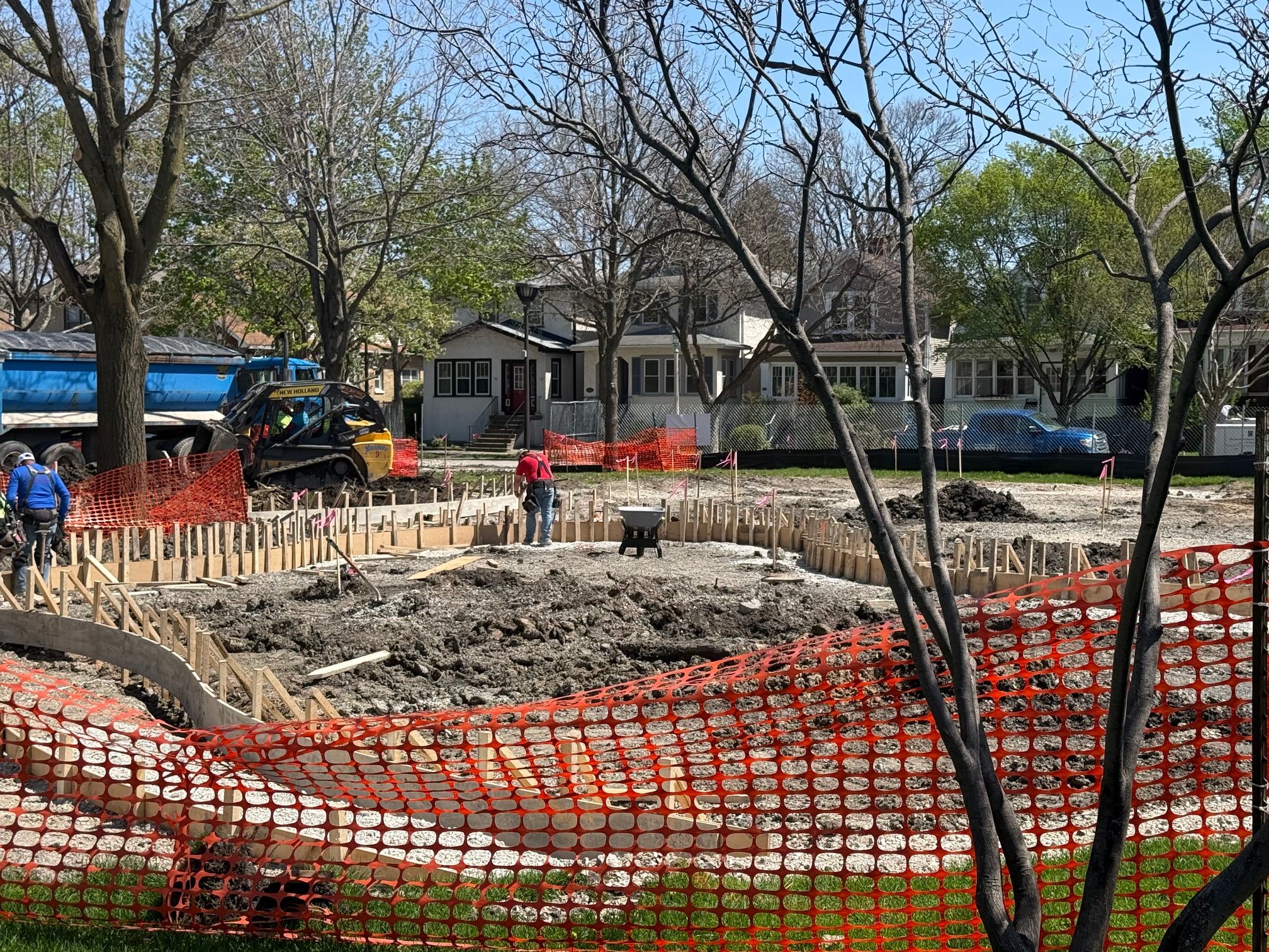 Construction workers and heavy machinery are present at a site for Longfellow Park (facilities_dir_ltg). Forms for concrete are set up, and orange