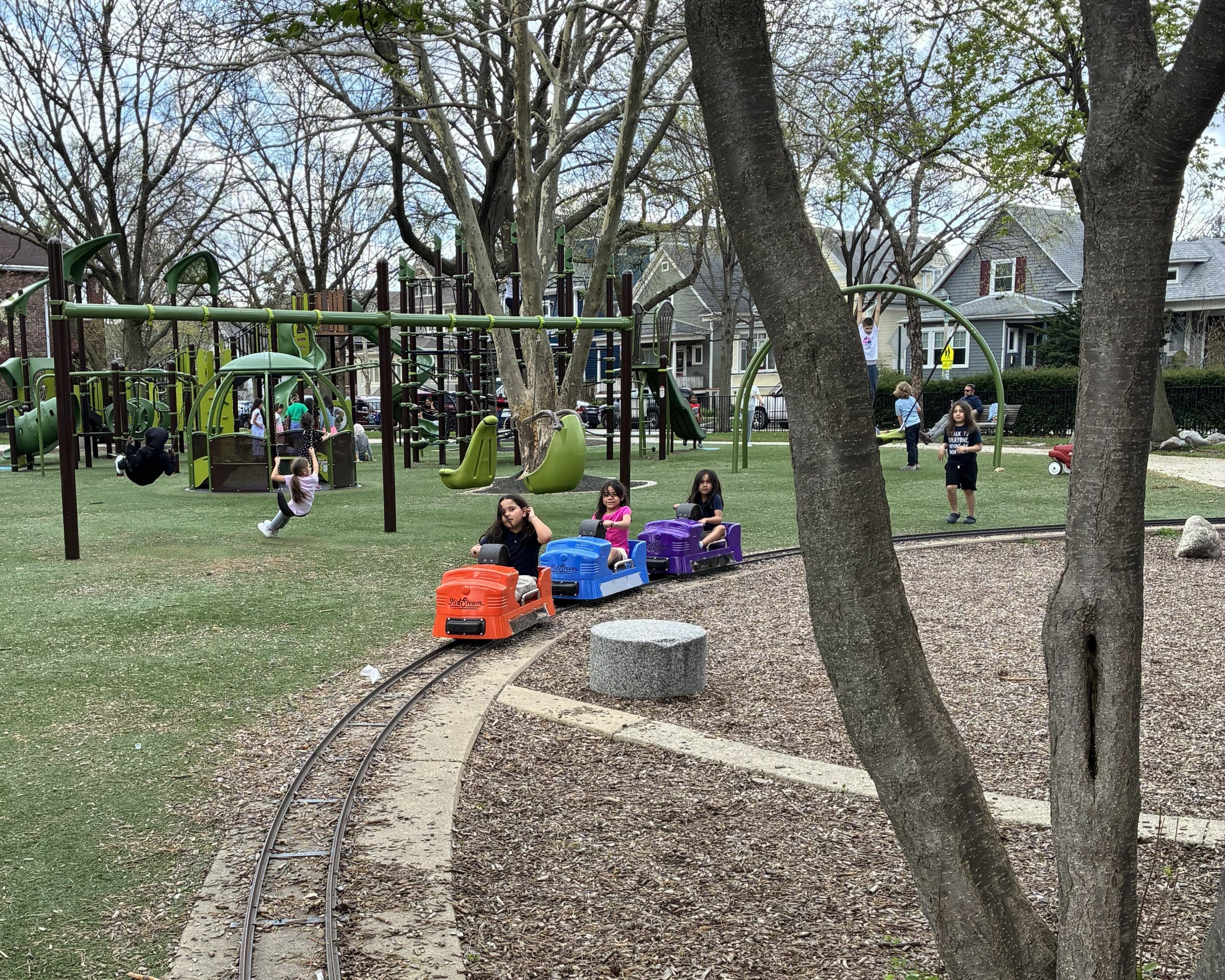 children sitting on orange, blue, and purple hand pedal train cars