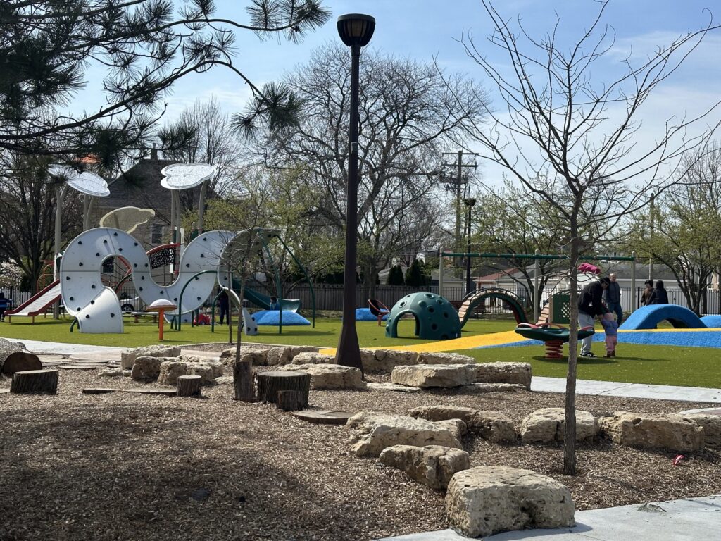 Barrie Park playground features a large spiral climbing structure, slides, swings, and a green dome climber on a bright