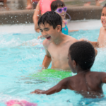 Two boys splashing and laughing in a swimming pool during a birthday party.
