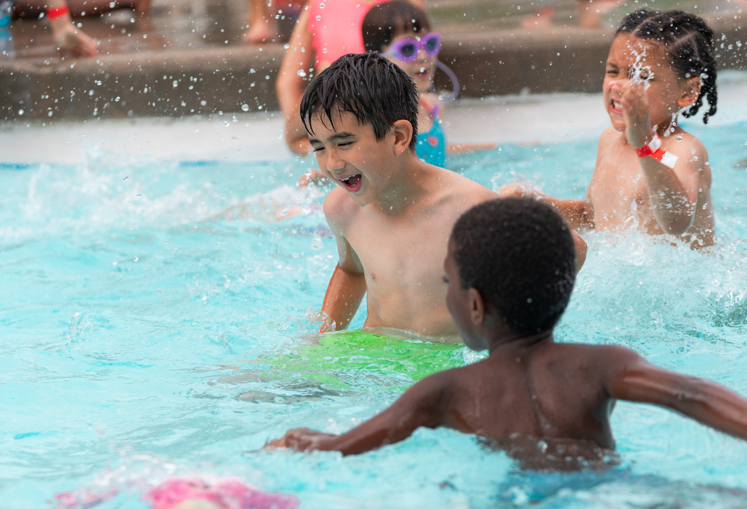 Two boys splashing and laughing in a swimming pool during a birthday party.