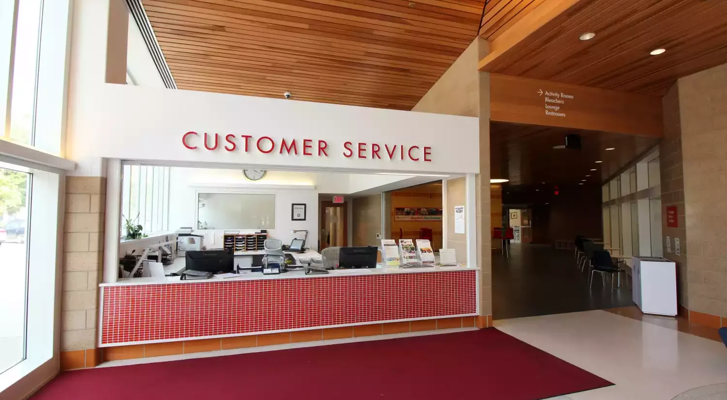 Customer Service desk with computers and brochures, with signage indicating directions to Activity Rooms, Bleachers, Lounge, and Restrooms.