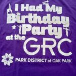 Purple t-shirt with white text: "I Had My Birthday Party at the GRC PARK DISTRICT of OAK PARK". Includes small gymnastics graphics.