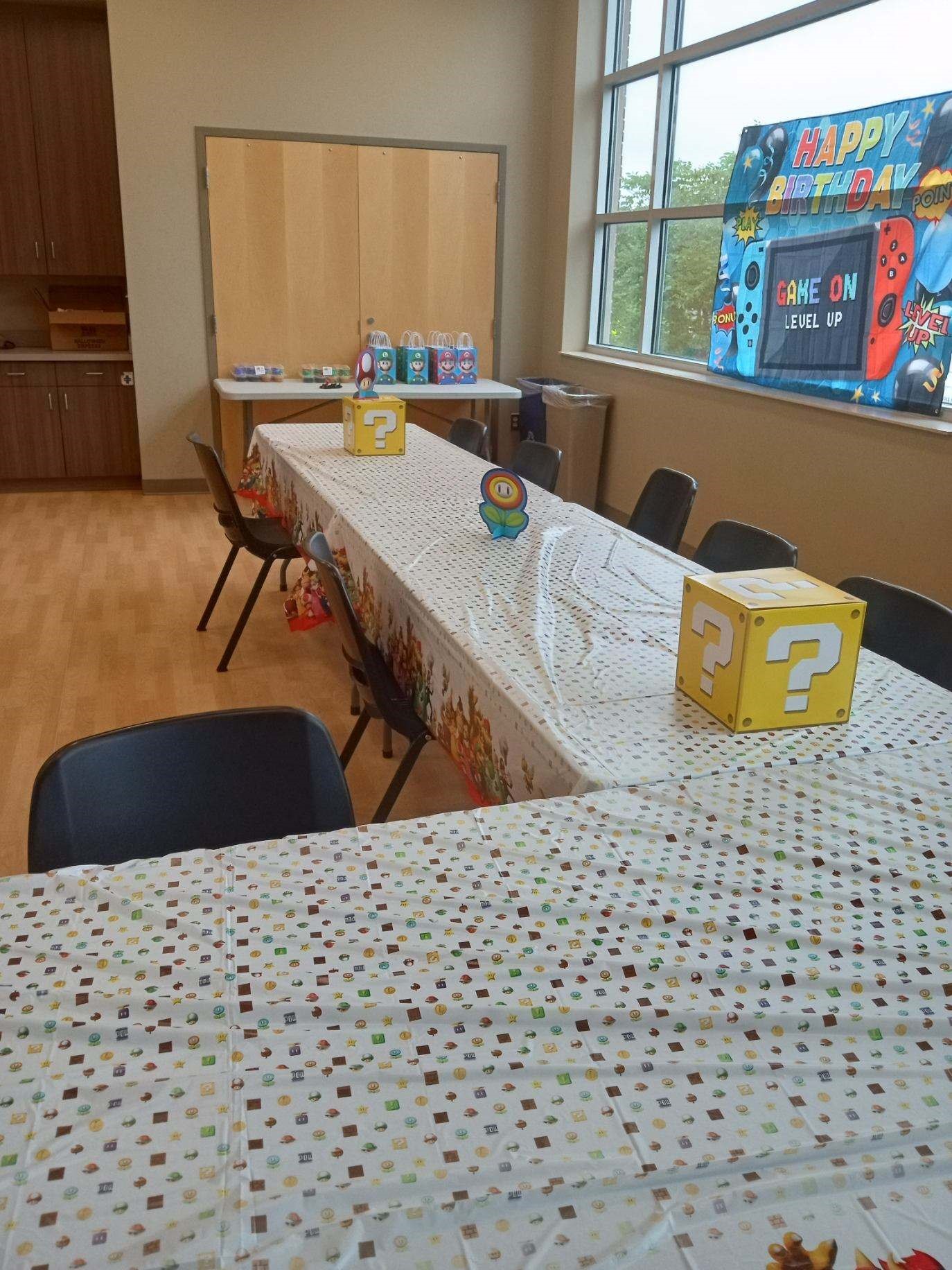 A long table is set for a Super Mario-themed birthday party with question block decorations and party favor bags.