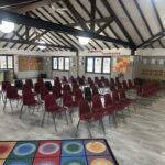 Chairs arranged in rows in a community room with a high, beamed ceiling and large windows.