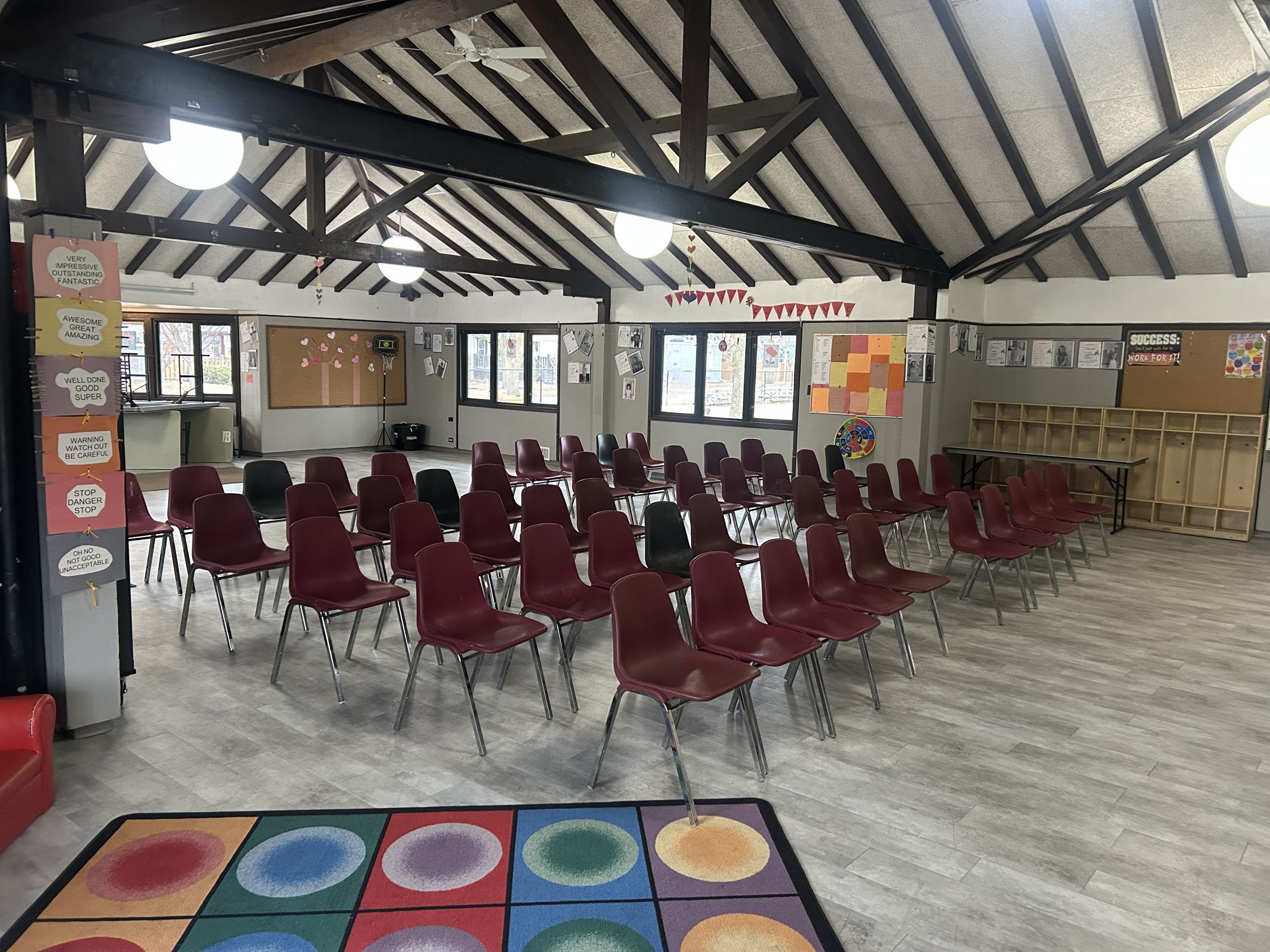 Chairs arranged in rows in a community room with a high, beamed ceiling and large windows.