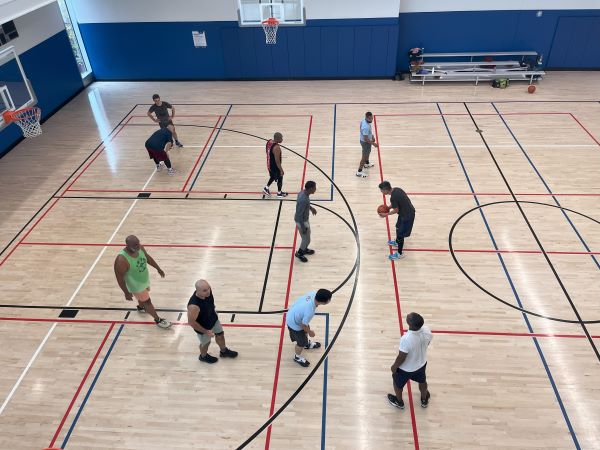 Several men playing basketball on an indoor court. One man is dribbling the ball while others are positioned around the court.