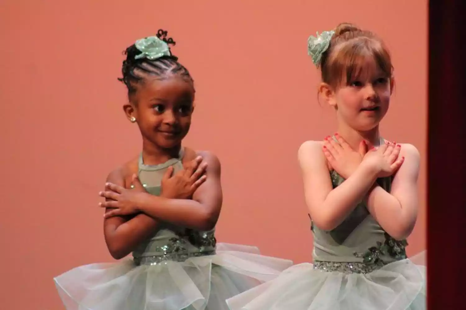 Two young ballet dancers in light green tutus with floral embellishments and hair ornaments perform on stage.