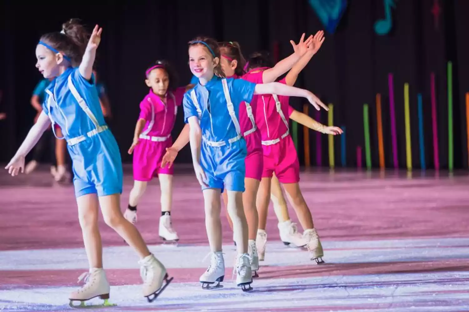 Young figure skaters in blue and pink costumes perform on ice during the Ice Show.